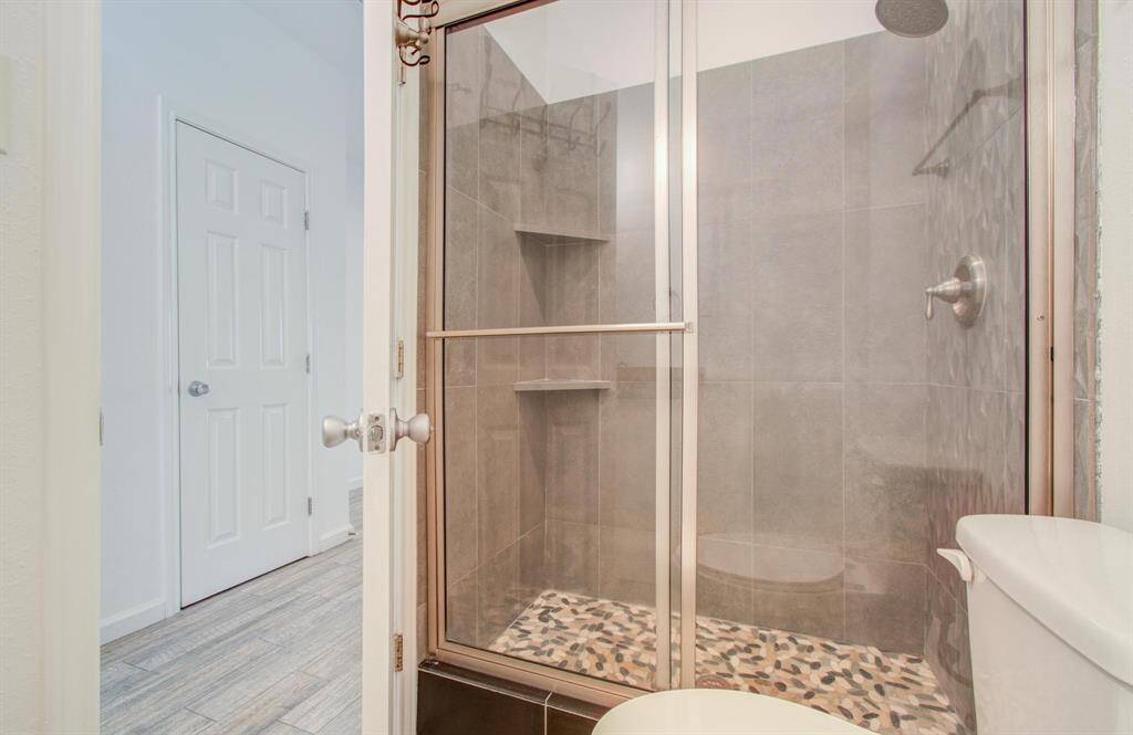 Modern tiled shower with sliding glass doors and a pebble stone floor, offering a sleek and stylish design.