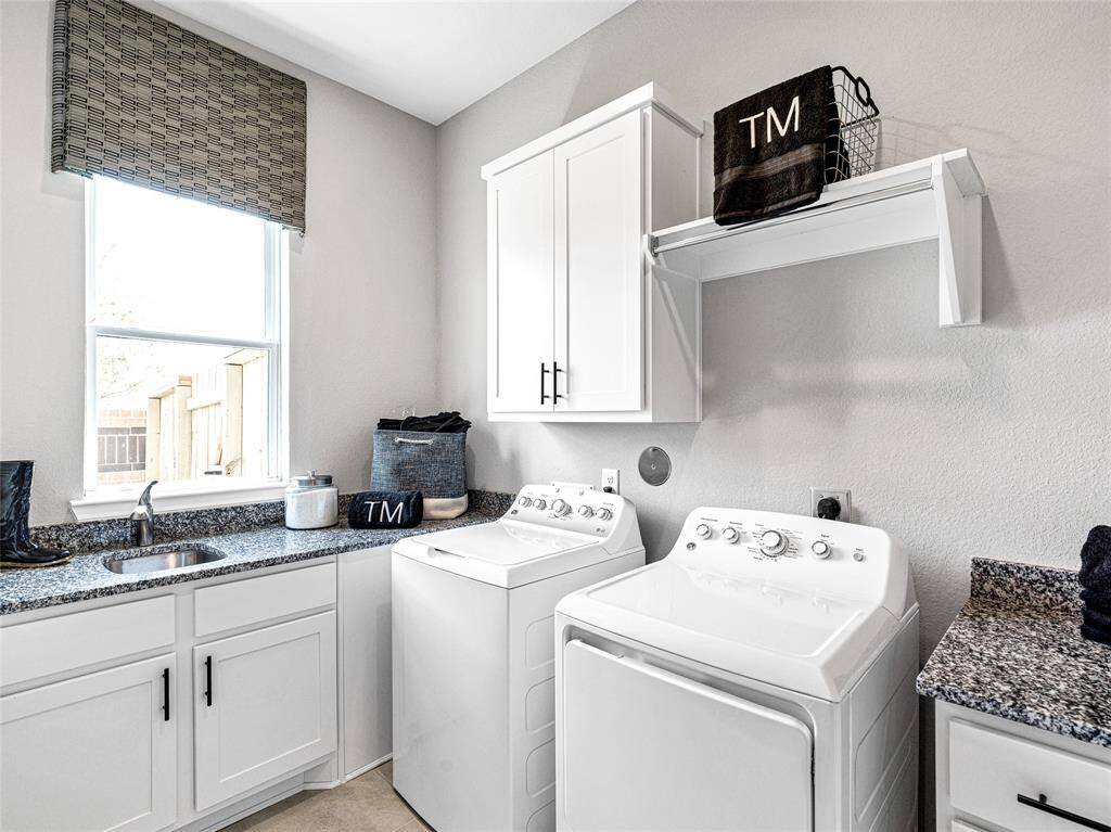 Bright and functional laundry room featuring white cabinetry, and modern appliances. A large window provides natural light, and there's ample storage space for convenience.