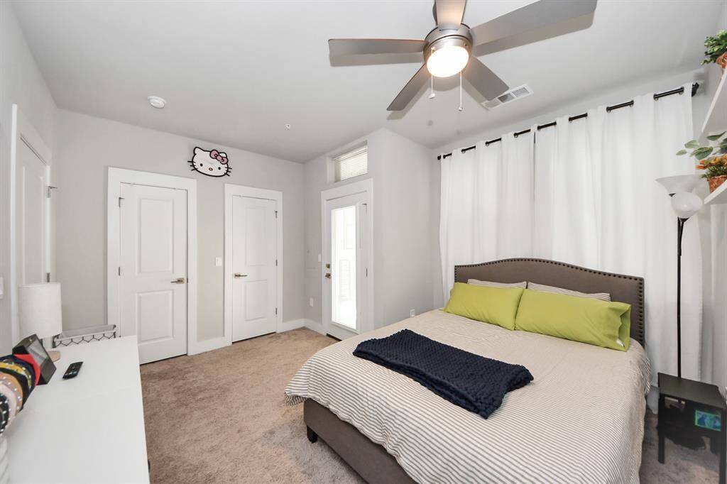 This bedroom is bright and cozy, featuring a neutral color palette with a plush carpet, ceiling fan, and ample natural light. It includes two closets and modern decor, creating a comfortable and inviting space.