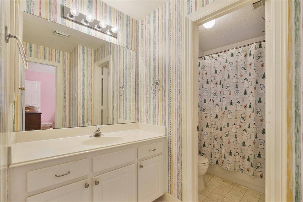 This Secondary Bathroom has tile floors, wooden cabinets, granite countertops, a large mirror, and a shower/tub combo.