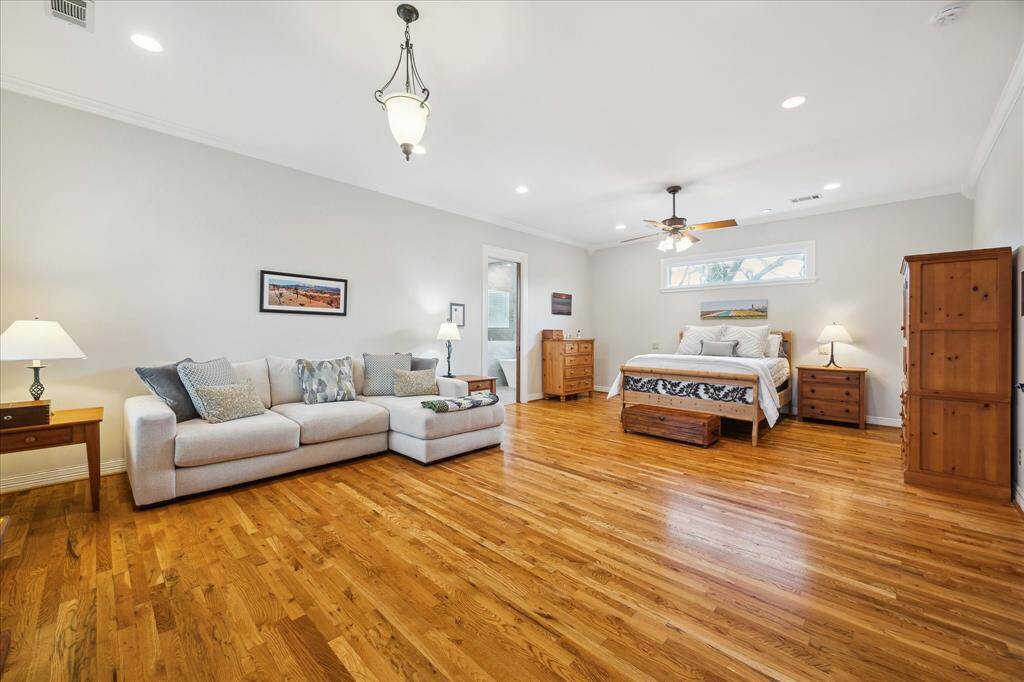 The expansive primary suite is a peaceful retreat, complete with wood flooring, recessed lighting, crown molding, a ceiling fan, and a fantastic sitting area.