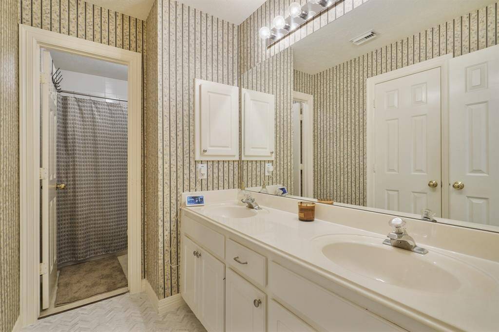 Secondary Bathroom with double sinks, white cabinets, granite countertops, a large mirror, and tile floors.