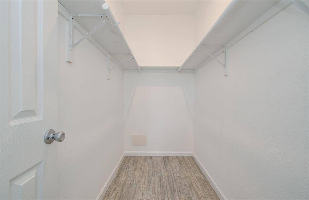 This is a spacious walk-in closet with white walls and vinyl flooring, featuring two long shelves and hanging rods for ample storage.