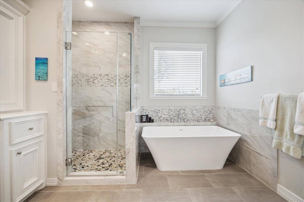 The primary bath also features a large soaking tub and a stunning shower with pebble stone flooring, exquisite tile work, and a sleek frameless glass door, creating a spa-like experience.