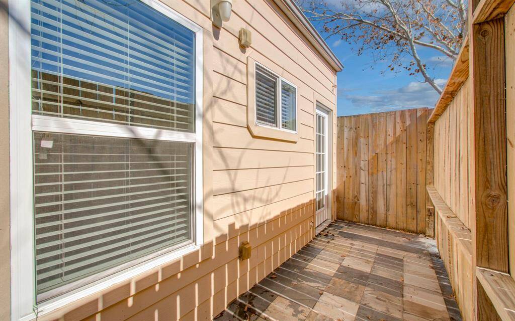 Cozy outdoor patio area with wood fencing and tile flooring, adjacent to the house with large windows and a glass door, offering a private space for relaxation.