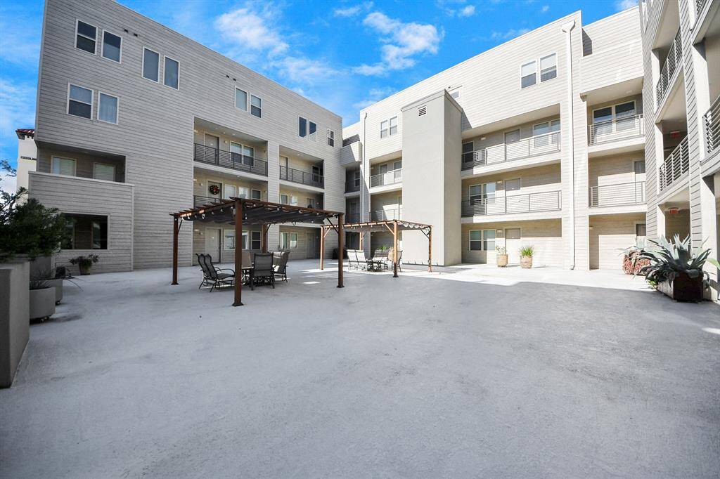 Modern condominium complex with a spacious, open courtyard. It features a seating area under a pergola. The area is well-maintained and offers a clean, inviting atmosphere.