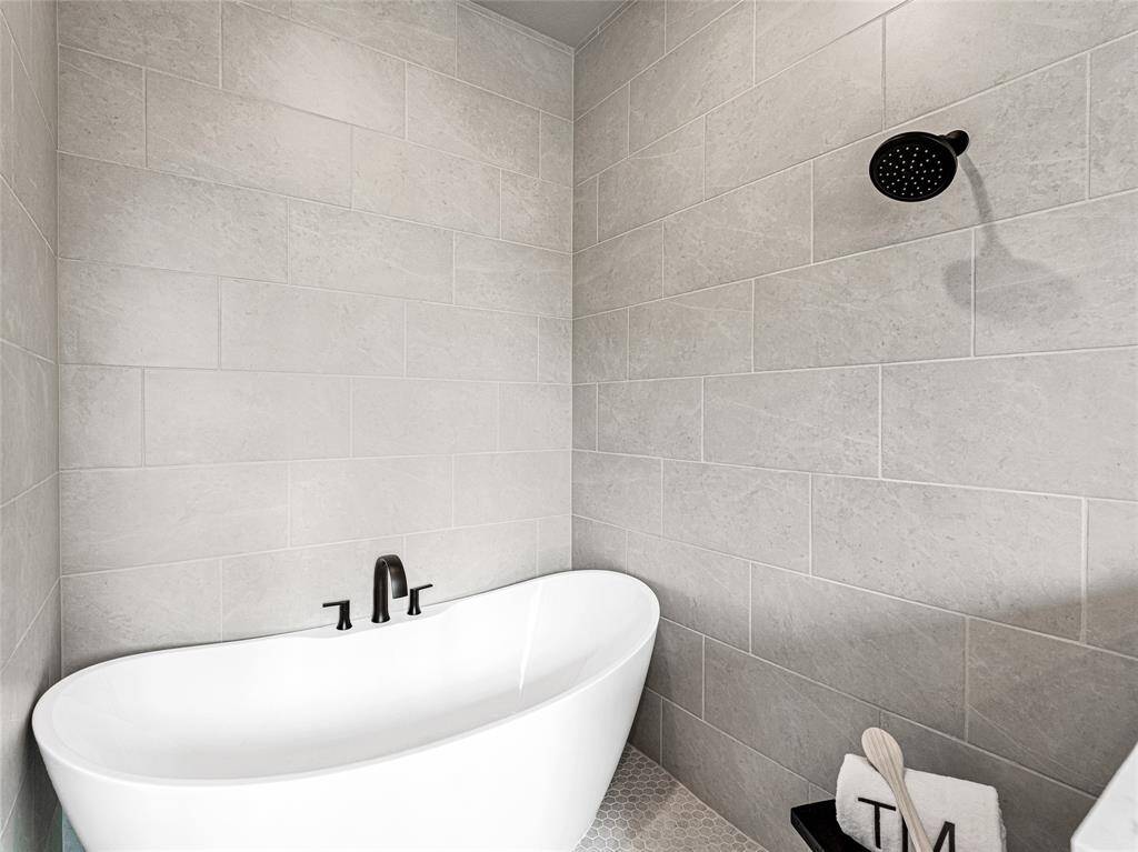 Walk in shower with sleek freestanding bathtub and modern black fixtures, set against elegant light gray tiled walls.