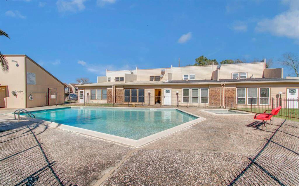 Another view of community pool area surrounded by a paved deck and fencing. Space includes chairs for lounging, offering a welcoming and relaxing environment.