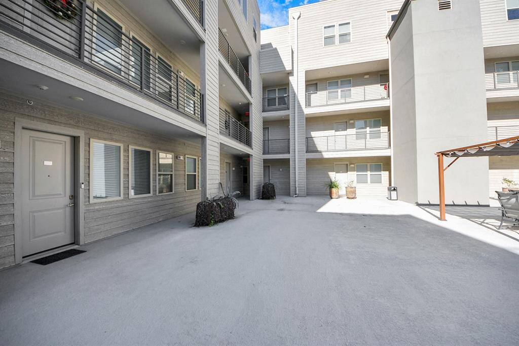 37 Unit complex courtyard with multiple stories, featuring balconies and large windows. The area is spacious and well-maintained, with a light neutral color scheme and some outdoor seating under a pergola.