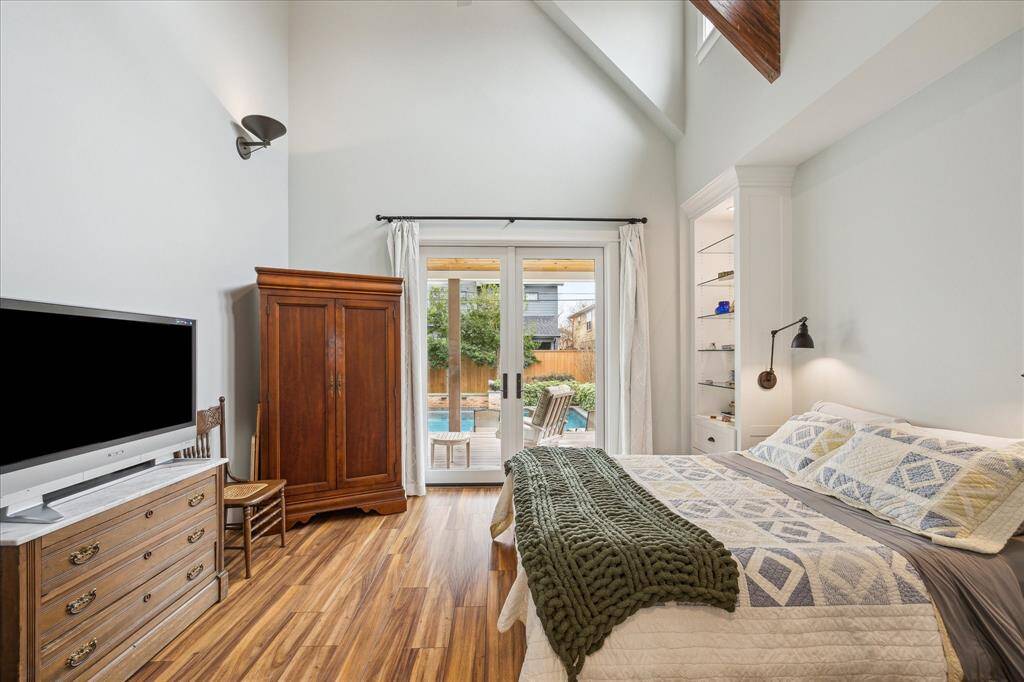 The spacious bedroom features double doors that open directly to the pool, a vaulted ceiling, and built-in shelving with elegant glass shelves, creating a bright and inviting retreat.