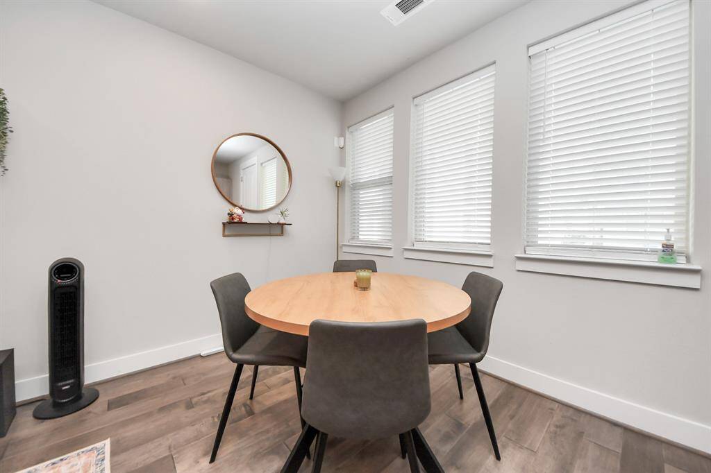 This cozy dining area is well-lit by three large windows with blinds. The space has a clean, minimalist design.