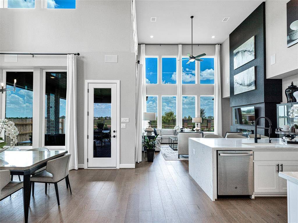 Open-concept living space with high ceilings and large windows, offering plenty of natural light.  The dining area is adjacent, and there's easy access to an outdoor space through glass doors.