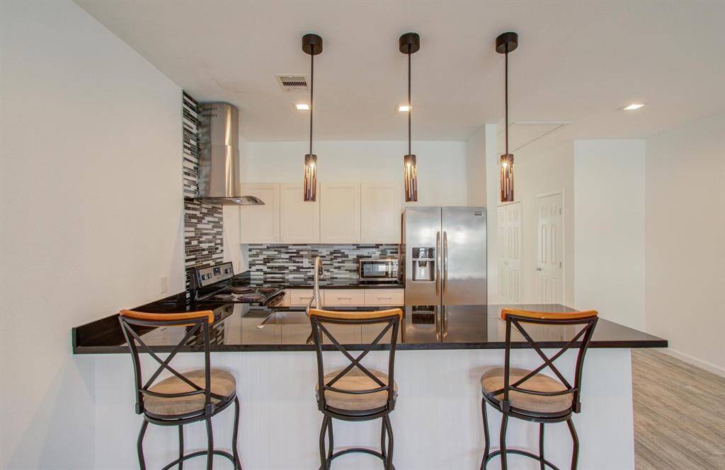 Modern kitchen with a sleek black countertop and bar seating. Features stainless steel appliances, stylish pendant lighting, and a contemporary backsplash.