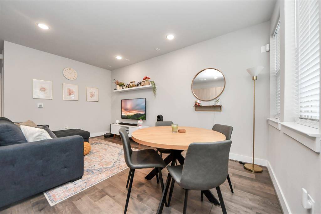 Cozy living and dining area, the room is well-lit with recessed lighting and has large windows providing natural light. The neutral color palette creates a welcoming atmosphere.