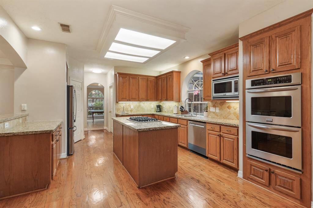 Host your next dinner party with confidence! This masterfully-equipped kitchen features a kitchen island with cooktop under a fantastic skylight, an abundance of cabinetry and hardware, under cabinet lighting, tons of counter space, granite countertops, recessed lighting, and stainless-steel appliances.