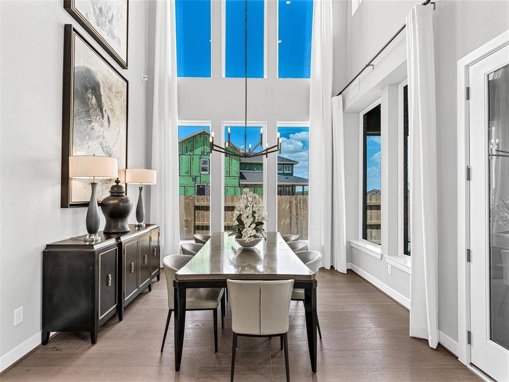This elegant dining room features high ceilings, large windows with abundant natural light, contemporary decor, and a spacious table, creating a welcoming and sophisticated atmosphere.