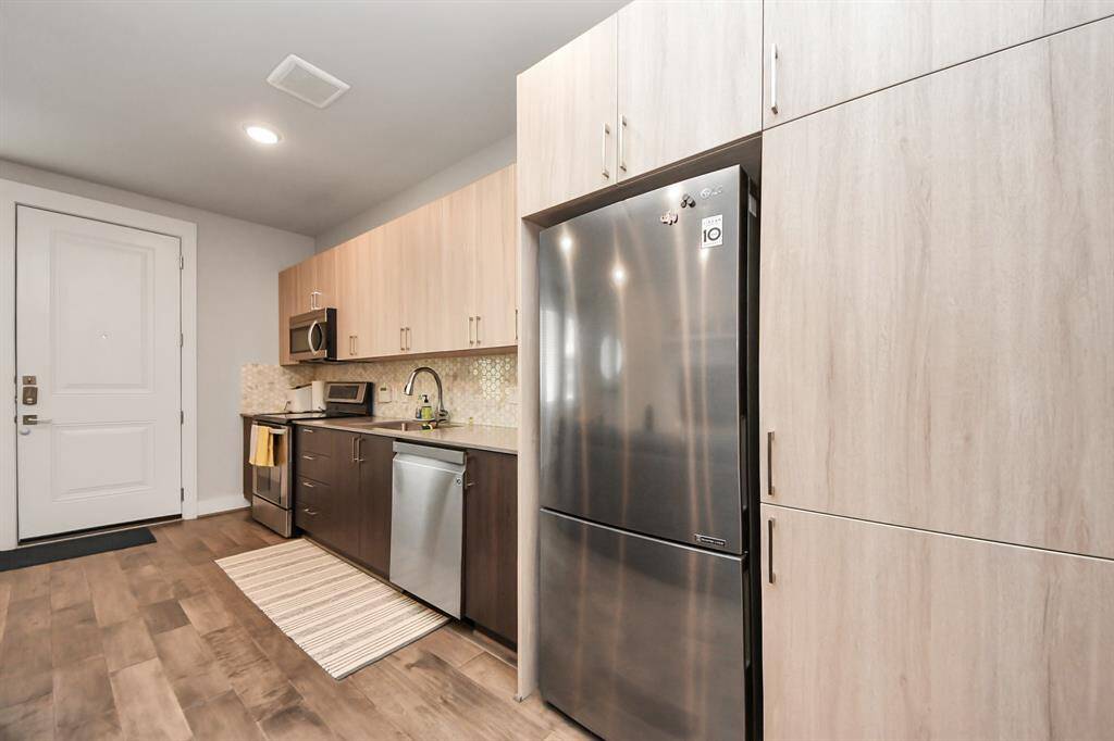 This modern kitchen features sleek stainless steel appliances, light wood cabinetry, and a stylish backsplash. The open layout offers ample storage and workspace, perfect for cooking and entertaining.