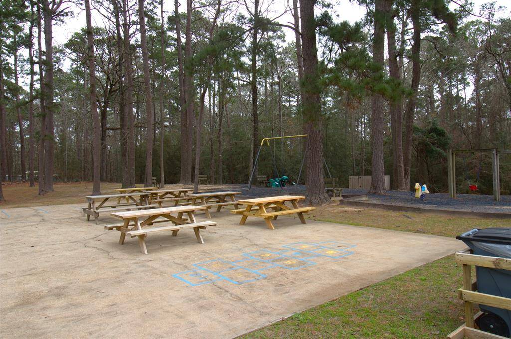 Discover a charming outdoor retreat featuring picnic tables, a children's play area, and a hopscotch court—all set within a serene wooded backdrop. Perfect for family fun and relaxation.