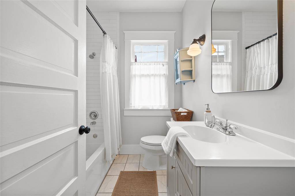 Modern Bathroom with school house sconces, tile flooring, and white subway tile in the shower/bathtub combo.  There is also a linen closet located behind the door.
