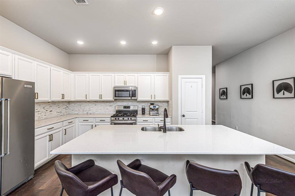 This modern kitchen features sleek stainless steel appliances, white cabinetry, and a large island with a built-in sink. The open layout is complemented by stylish barstool seating and decorative wall art, creating a welcoming and functional space.