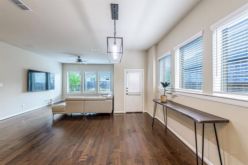 Bright and spacious living room with hardwood floors, large windows, and a modern light fixture. Features a mounted TV, cozy sectional sofa, and a sleek console table. Perfect for entertaining and relaxation.