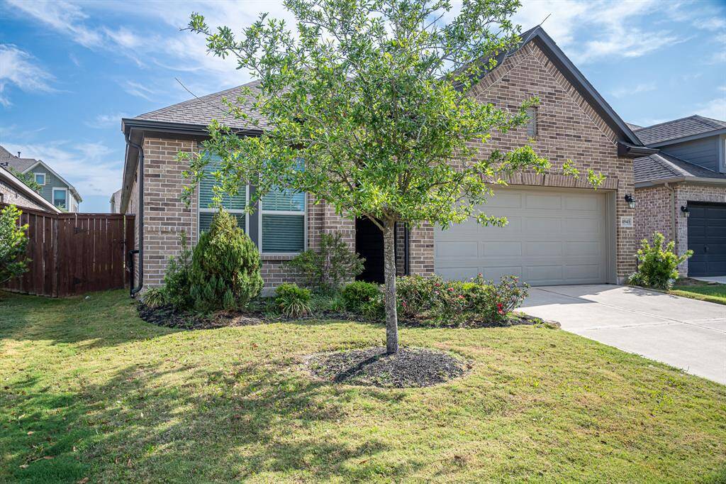 Charming single-story brick home with a neatly landscaped front yard, featuring a young tree and shrubs. It includes a two-car garage and has a welcoming, well-maintained exterior.