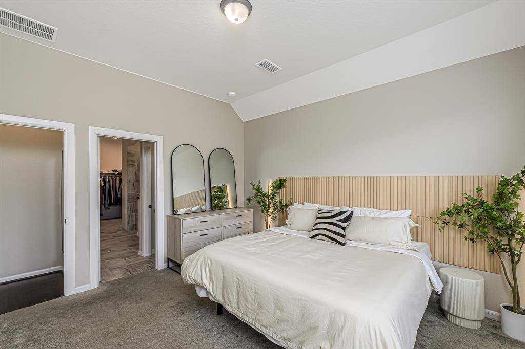 This spacious bedroom features a neutral color palette, plush carpeting, and a stylish wood accent wall. It includes a large walk-in closet and modern furnishings, offering a comfortable and inviting atmosphere.