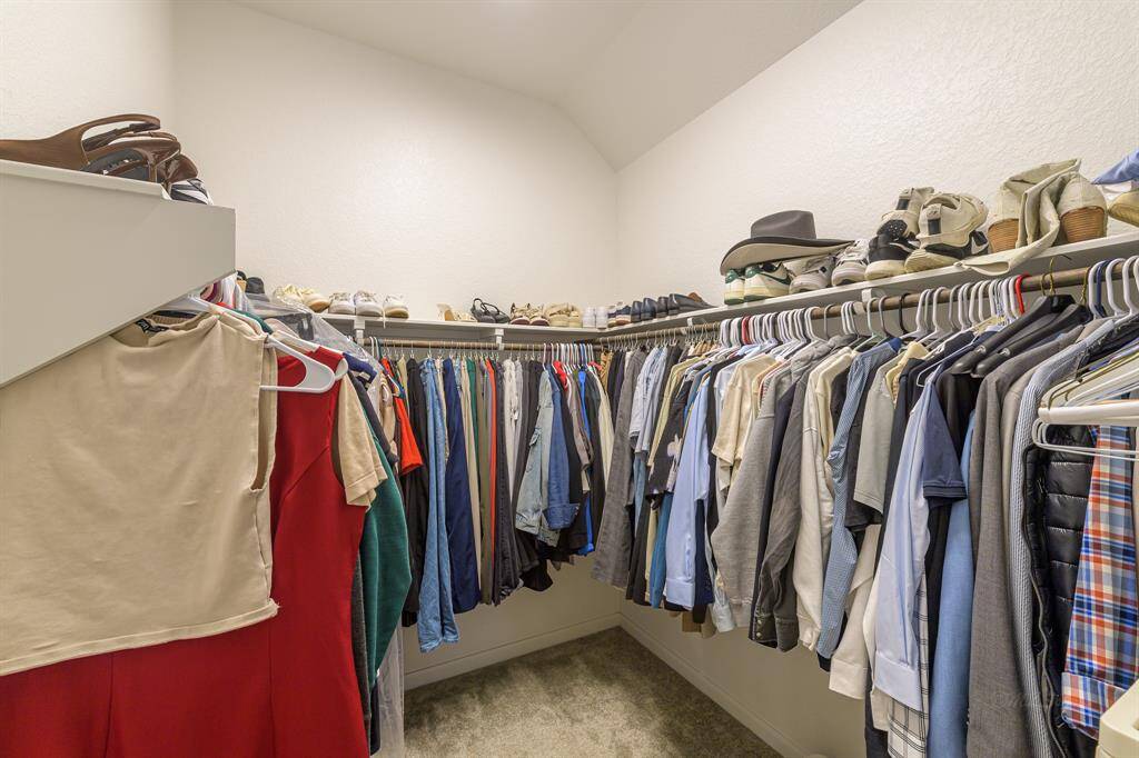 This spacious walk-in closet features ample hanging space and shelving, perfect for organizing clothing and shoes. Ideal for maintaining a tidy and accessible wardrobe.