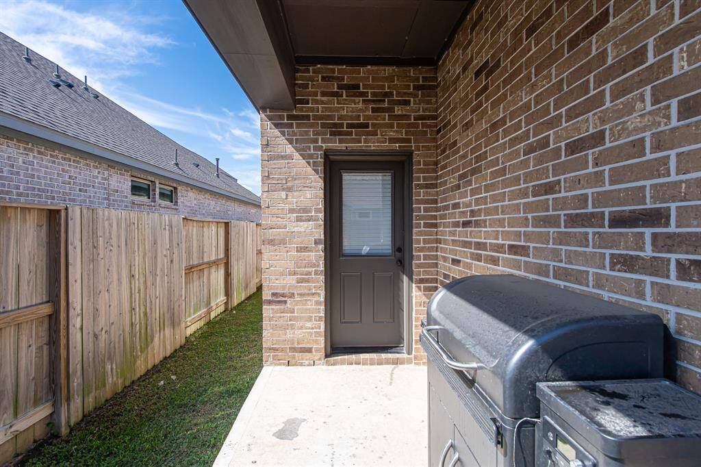 This photo shows a cozy outdoor space with a brick exterior wall, a back door, and a fenced yard. There's a BBQ grill on a concrete patio, ideal for outdoor cooking and entertaining.
