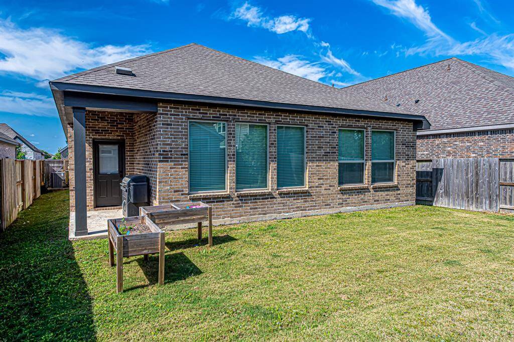 This photo shows a brick house with multiple windows and a small backyard. The yard is fenced and features two raised garden beds. The space is well-maintained and offers potential for outdoor activities.