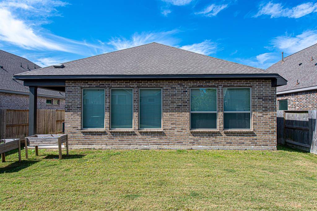 This photo shows the backyard of a brick house with a sloped roof and five large windows. The yard is grassy and fenced, providing a private outdoor space.
