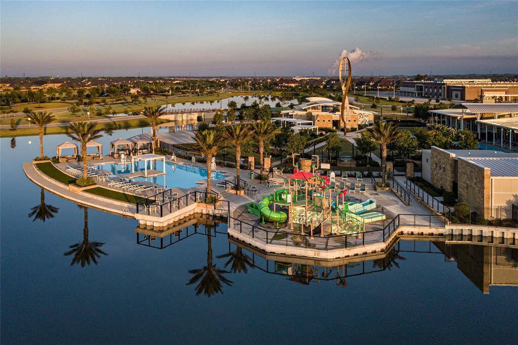 This photo showcases a luxurious waterfront community center with a pool, playground, and modern amenities, surrounded by lush landscaping and serene water views.