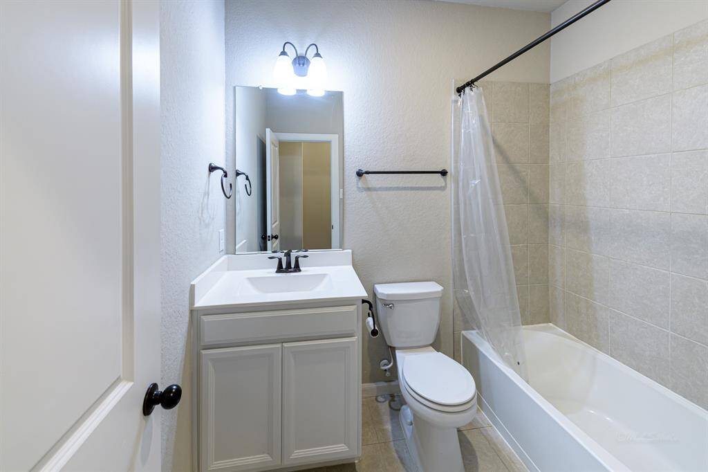 This is a bright, modern bathroom featuring a vanity with a large mirror, a toilet, and a bathtub with a shower. The space is well-lit and has neutral tilework, offering a clean and functional design.