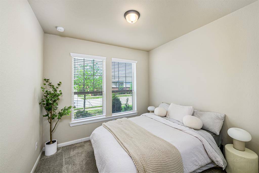 Cozy bedroom with neutral tones, featuring a large window for natural light, soft carpet, and simple, modern decor. Ideal for a peaceful retreat.