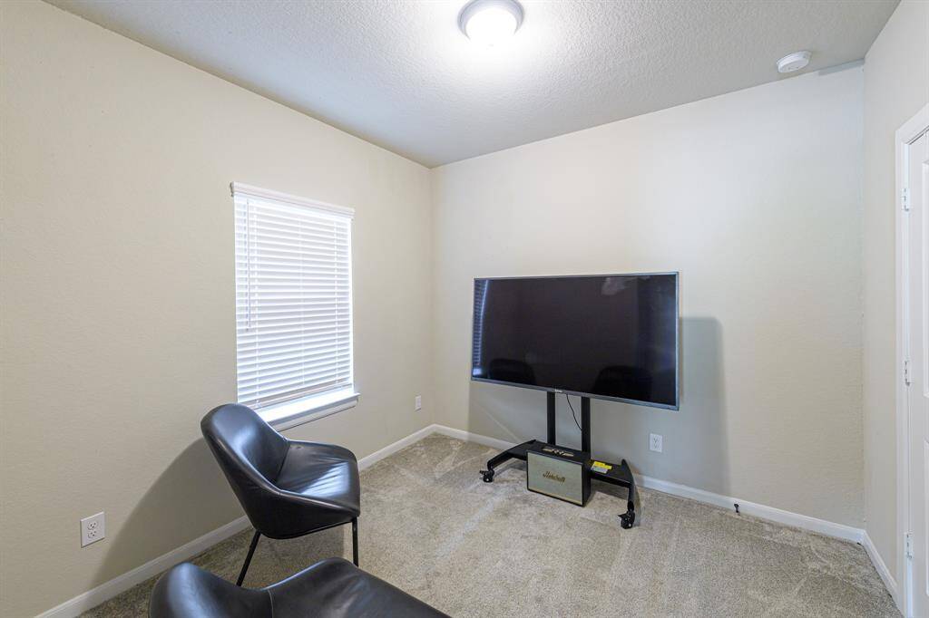 Cozy room with neutral walls, featuring a window with blinds, carpeted floor, modern chairs, and a mounted TV, ideal for a small entertainment area.