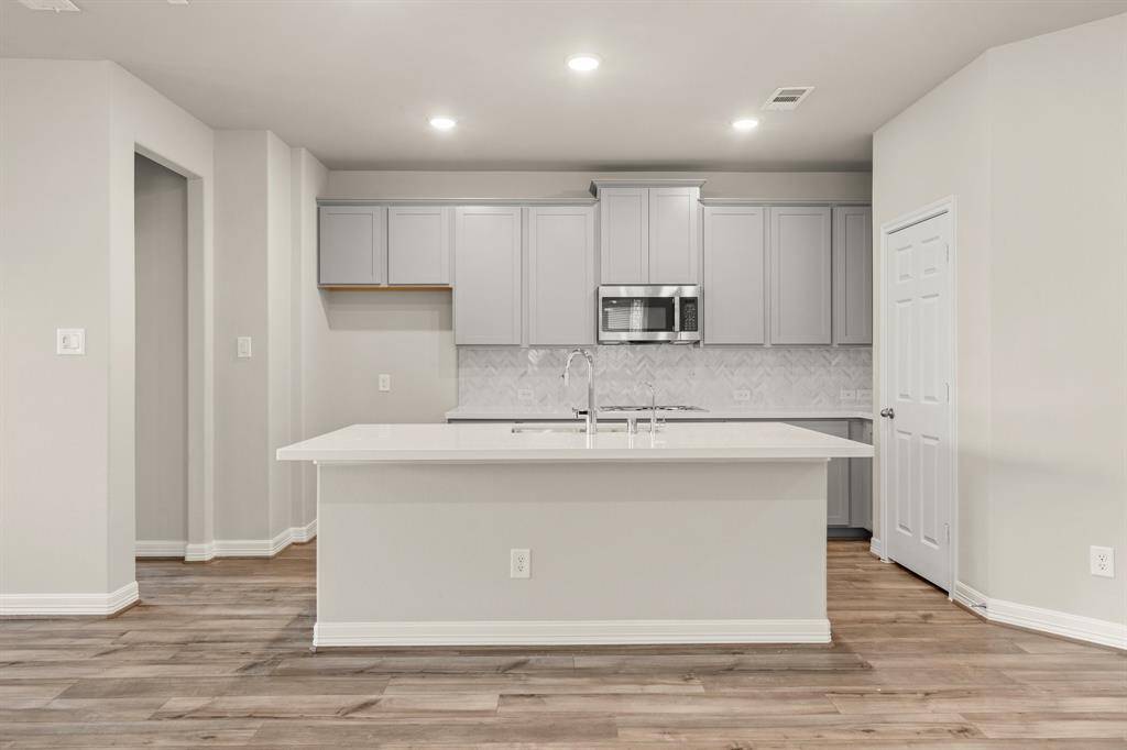 This light and bright kitchen features a large quartz island, white cabinets, a large sink overlooking your family room, recessed lighting, and beautiful backsplash.