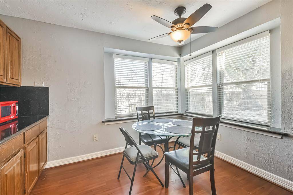 Bright breakfast nook with large windows, hardwood floors, and a cozy dining setup. Features a ceiling fan and built-in cabinetry with a countertop.