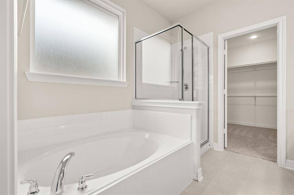 This additional view of your primary bathroom features tile flooring, fresh paint, walk-in shower, a separate garden tub, and a large walk-in closet.