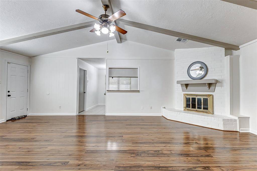 A white-painted brick gaslog fireplace with a custom mantle serves as a striking focal point in the room, adding both charm and warmth. Above, a ceiling fan ensures comfortable air circulation, enhancing the overall comfort and flow of the space.