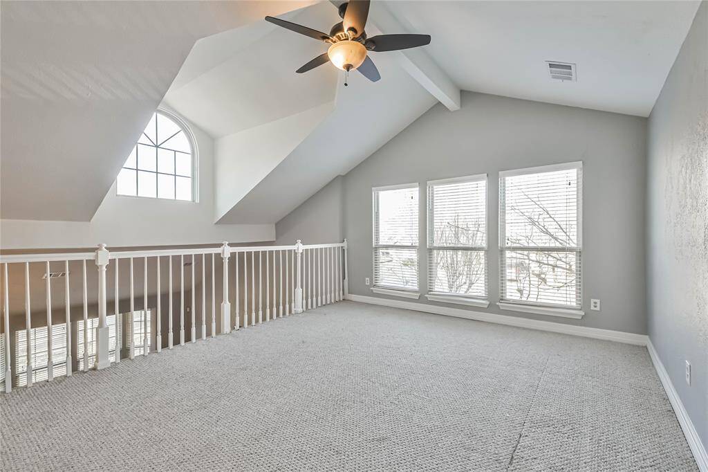 This spacious loft features vaulted ceilings, a large arched window, ample natural light, and a ceiling fan, offering a bright and airy atmosphere. Perfect for a home office or cozy retreat.