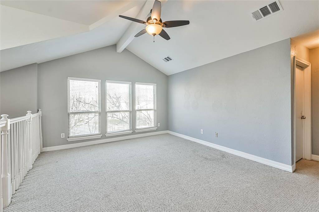 This bright, spacious room features high vaulted ceilings, large windows for natural light, neutral walls, and cozy carpet, making it an inviting and versatile space.