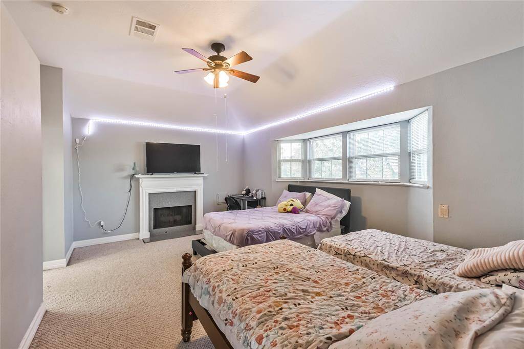 This room features a high vaulted ceiling with a modern ceiling fan, three large windows providing natural light, and neutral carpeting. It includes a railing overlooking an open space and a doorway leading to an adjacent area.