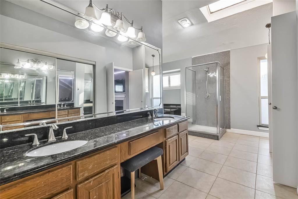 Spacious bathroom with double sinks and a large, granite-topped vanity. Features a glass-enclosed shower and ample natural light from a skylight and windows.