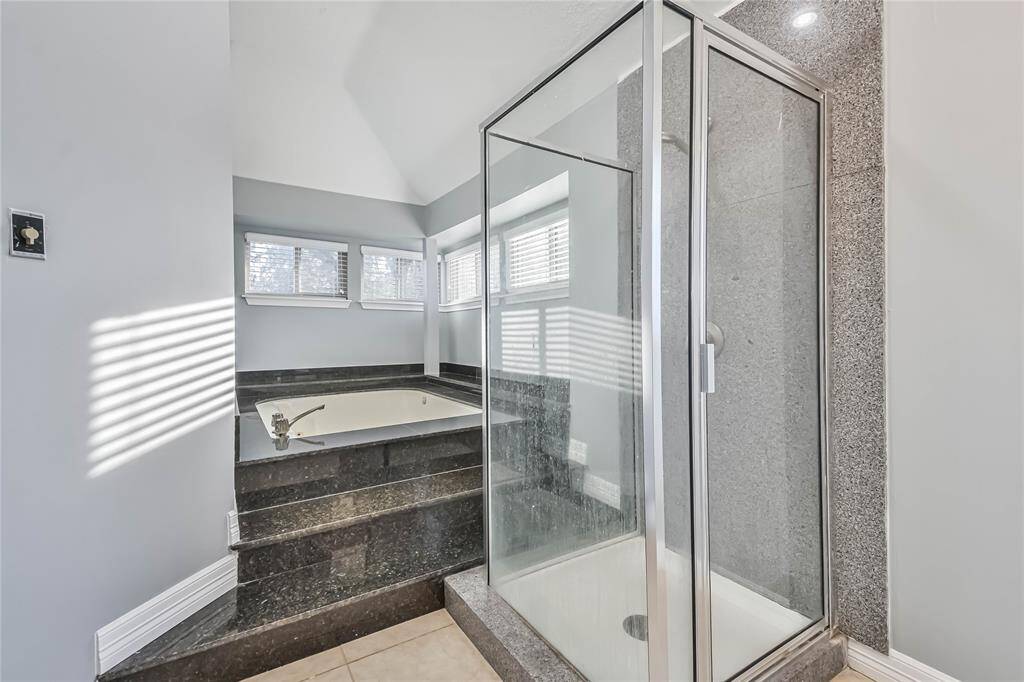 This bathroom features a spacious corner bathtub with granite steps and a separate glass-enclosed shower, accented by natural light from multiple windows.