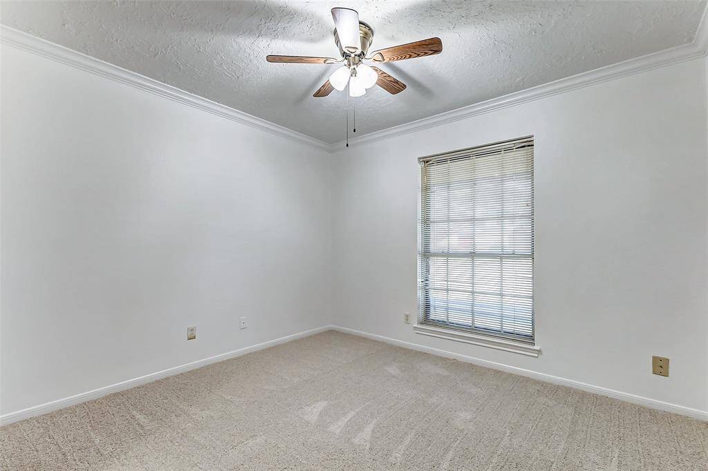 Guest bedroom number four features elegant crown molding, fresh decorator paint, and newly installed carpet, creating a welcoming atmosphere. A ceiling fan adds comfort, while a large window overlooks the front yard, allowing natural light to brighten the room.