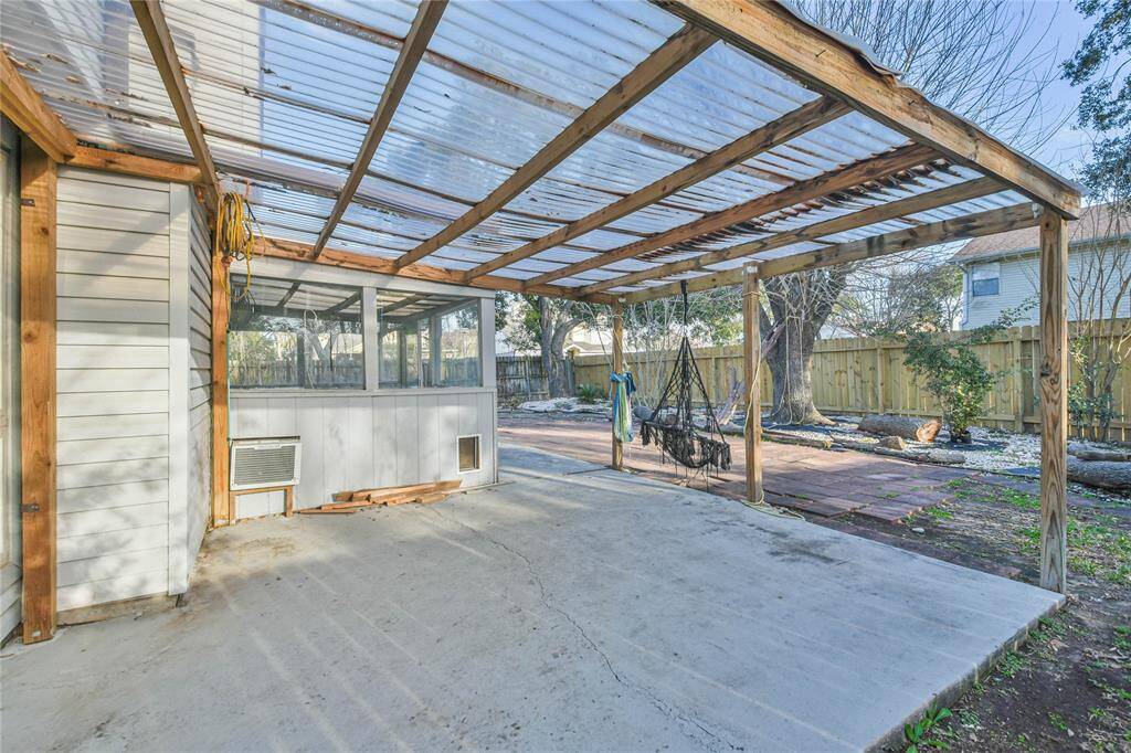This photo shows a spacious backyard area with a covered patio featuring a clear roof and wooden framework. There's ample space for outdoor seating and relaxation, complemented by a fenced yard and some greenery.