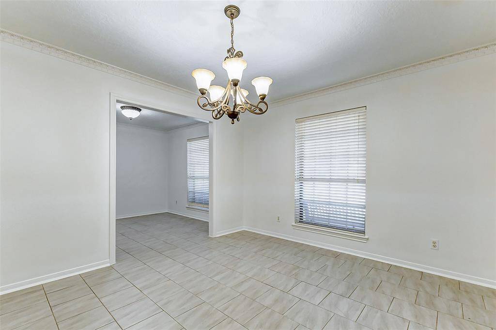 The formal dining area is adorned with an elegant chandelier that hangs overhead, complemented by classic crown molding, fresh paint, and neutral tile floors. With ample space for a large dining table, chairs, and even a china hutch, this room is perfect for hosting gatherings both big and small.