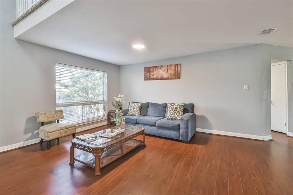 Bright, cozy living room with hardwood floors, featuring a large window, comfortable seating, and modern decor. Perfect for relaxation and entertaining.