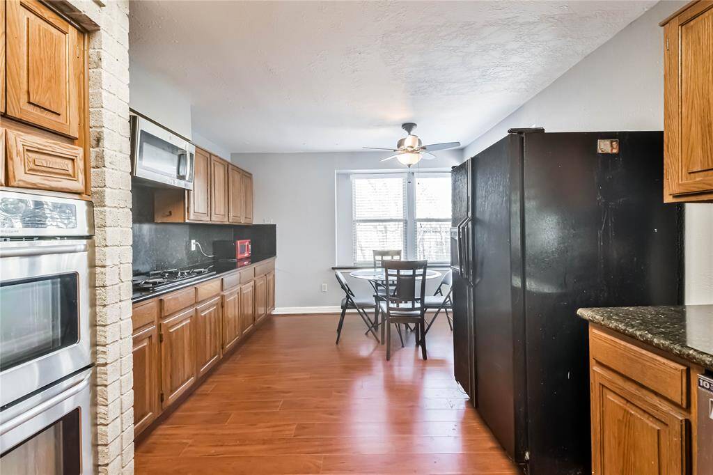 Spacious kitchen with wood cabinetry, granite countertops, and stainless steel appliances. It features a built-in oven, a gas cooktop, and a ceiling fan. There's ample natural light from the large windows facing the dining area.