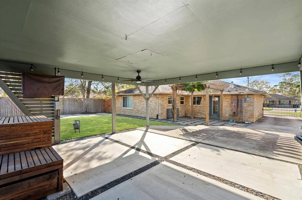 A large carport provides ample space for two cars, secured by a driveway gate. Carport also features a 220v outlet for EV charging, along with a ceiling fan and TV setup, perfect for entertaining large outdoor gatherings.